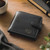 A black leather wallet with the initials "RG" and a Visconti logo embossed on the front. A cup of coffee and part of a plant  are also visible on a wooden surface.