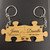 Two interlocking wooden puzzle piece keychains with silver metal rings. The left piece is engraved with the name James and the date 18th July 2016. The right piece features the name Danielle and the date 18th July 2016, with two small red hearts.