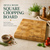 A square Hevea wood chopping board with a light brown grain pattern and the engraved text David's Kitchen. The board is displayed with a small bowl of peppercorns, garlic cloves, a sprig of rosemary, and fresh red tomatoes.