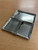 A rectangular silver-toned metal cigarette case with a hinged opening. The interior features a polished finish with a textured, cross-hatched pattern on the panels and a central metal bar designed to hold items securely in place when closed.