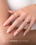 Elegant manicure featuring glossy, softly rounded almond-shaped nails in a delicate milky pink shade. The image showcases a smooth, natural-looking pink finish complemented by delicate gold rings and light blue denim, highlighting the feminine manicure style associated with Makear 605 Hybrid Gel Polish.