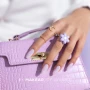 Professional manicure featuring neatly shaped purple nails decorated with delicate coloured speckles and subtle shimmering elements. The manicure showcases a playful, decorative purple nail look inspired by Makear 623 Joy Hybrid Gel Polish.
