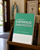 The Big Book of Catholic Answers displayed in a wooden literature rack inside a Catholic church vestibule, with a Marian statue and stained glass in the background.