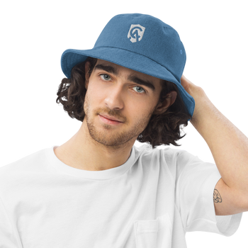 A young man wears the Catholic Answers denim bucket hat, smiling outdoors with a casual, confident vibe.