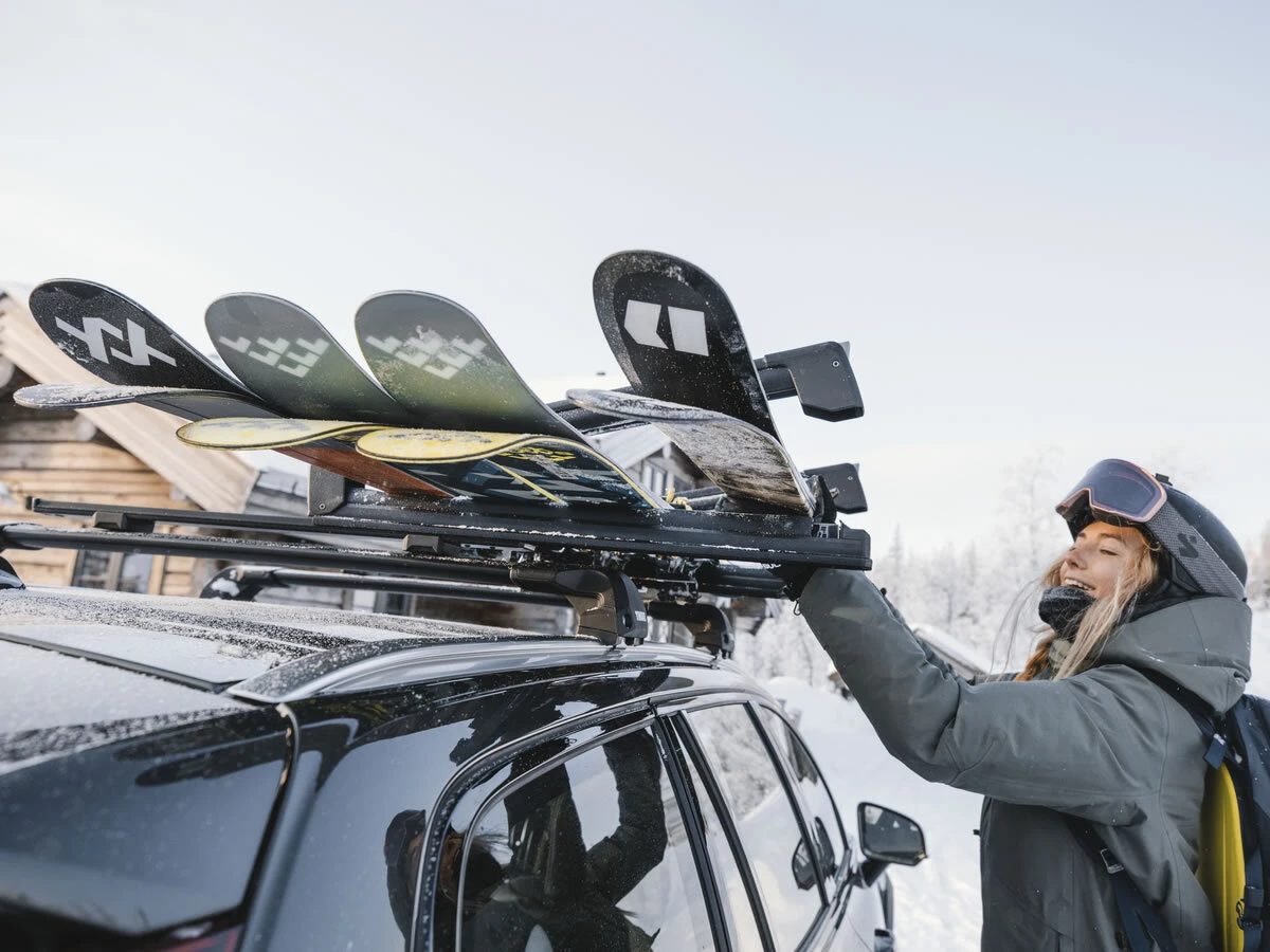 Skis secured to a roof carrier as a rider loads equipment in snowy conditions