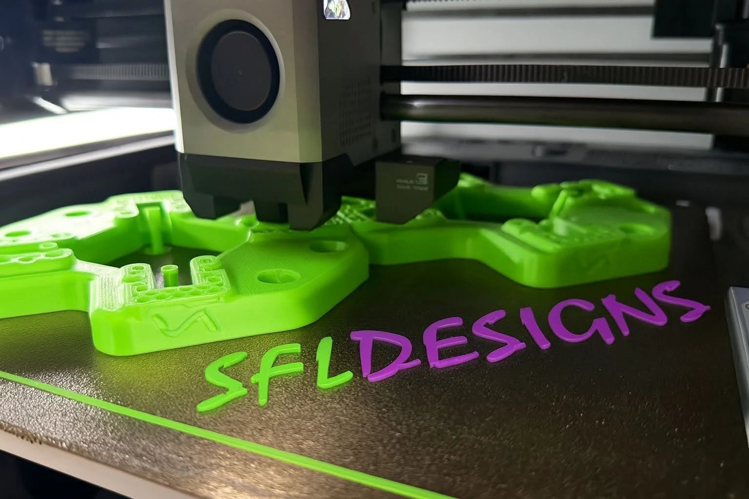 A green SFL mount printing, with SFL DESIGNS spelled out in printed letters on the build plate