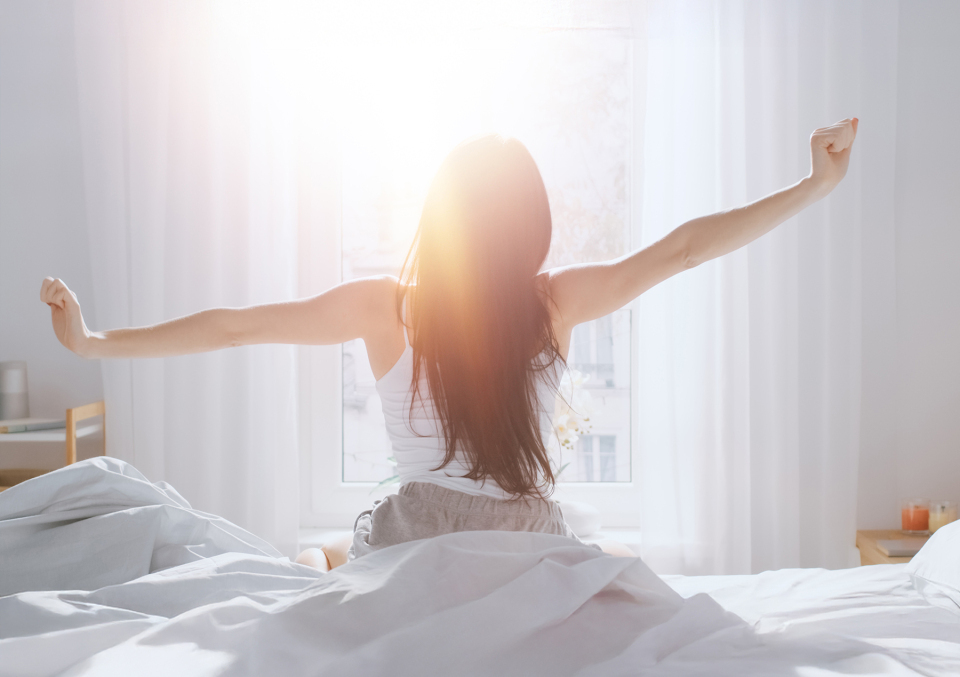 Woman waking up on her DwellSleep mattress and stretching in front of a window
