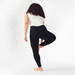 Person with brown curly shoulder length hair and dark skin shown mid yoga pose wearing black solid color organic cotton ankle base layer leggings.