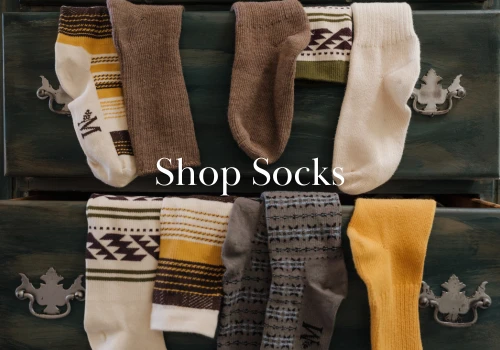 Image of socks draped over dresser drawer with overlayed text that reads "Shop Socks"