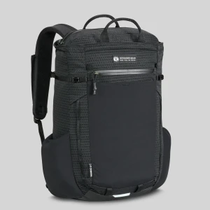 Looking at the corner of the backpack standing up against a white backdrop. The backpack is black and rectangular and is shown to have a front waterproof zip, 2 vertical daisy chains, and a large front mesh pouch on the bottom three quarters of the backpack. Also pictured are the large carry handles on top of the backpack.