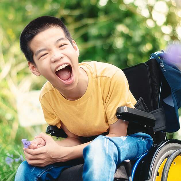 Happy boy in wheelchair smiling with excitement outdoors in summer.