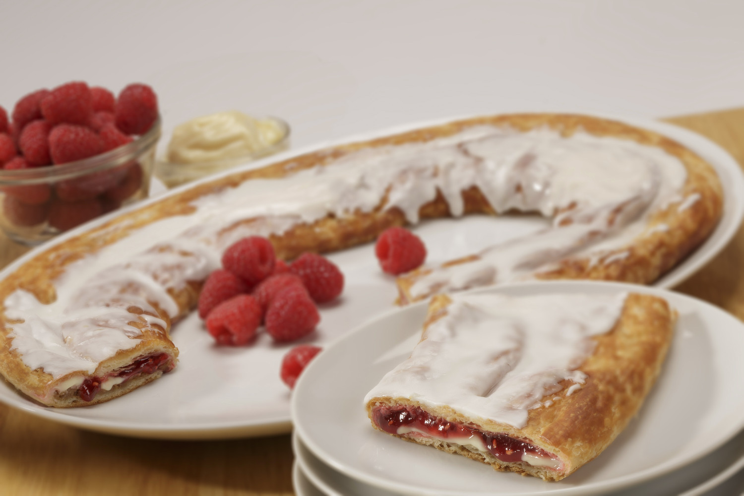 Raspberry Cheesecake Kringle on white plate, slice on smaller plate surrounded by raspberries.