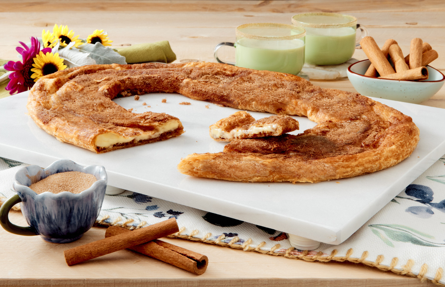 Churro Kringle on a white marble cutting board with a piece cut out.