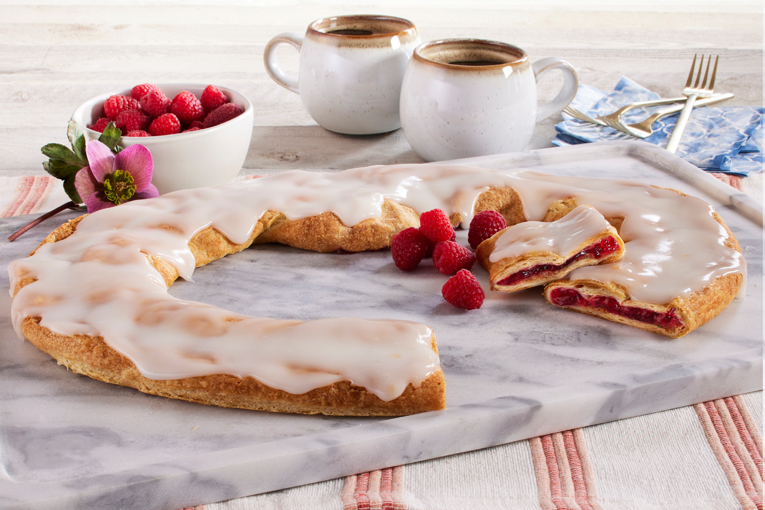 Raspberry kringle on a marble cutting board with raspberries and coffee next to the kringle.