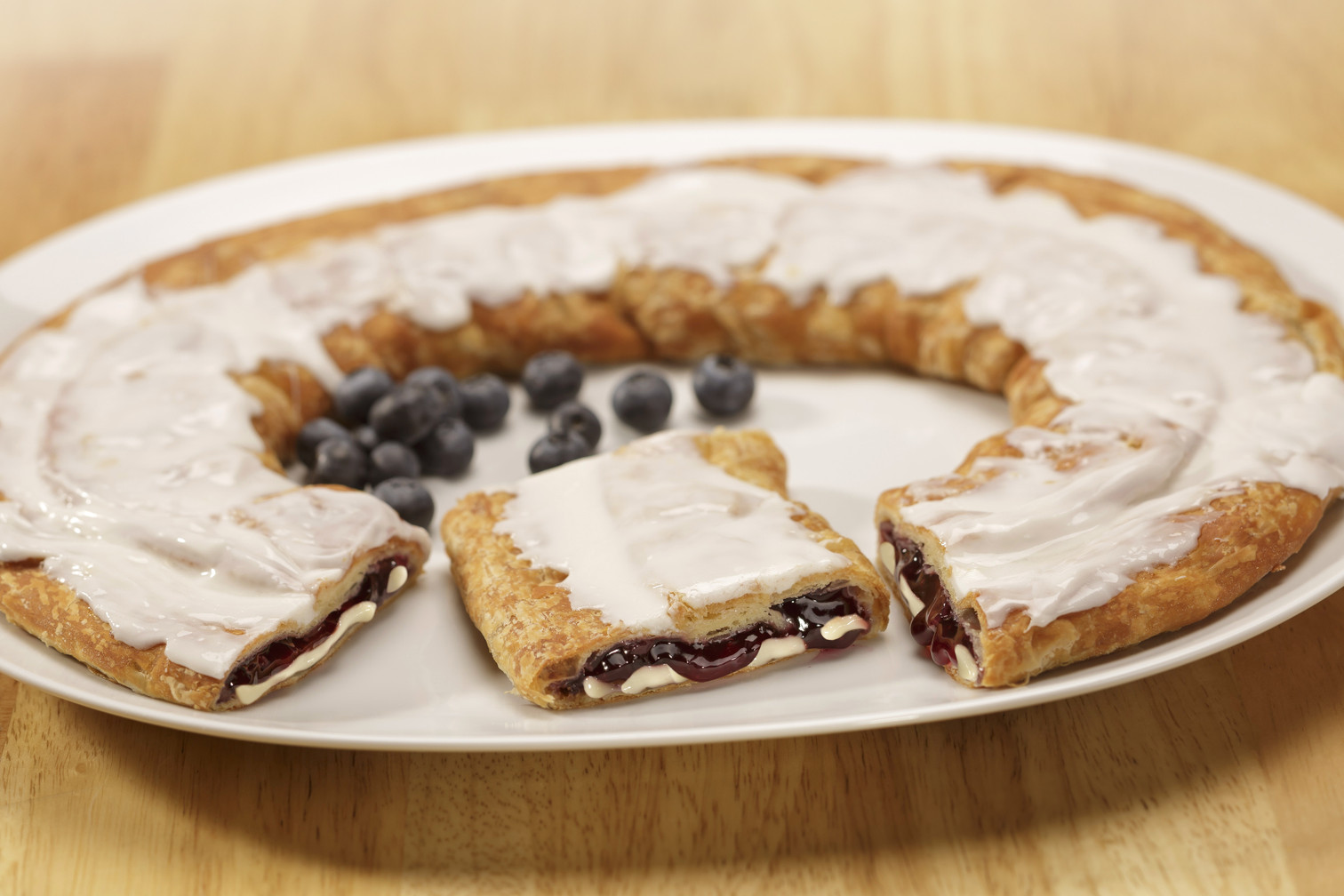 Blueberry Cheesecake Kringle sitting on a white plate with a piece cut out and some blueberries.