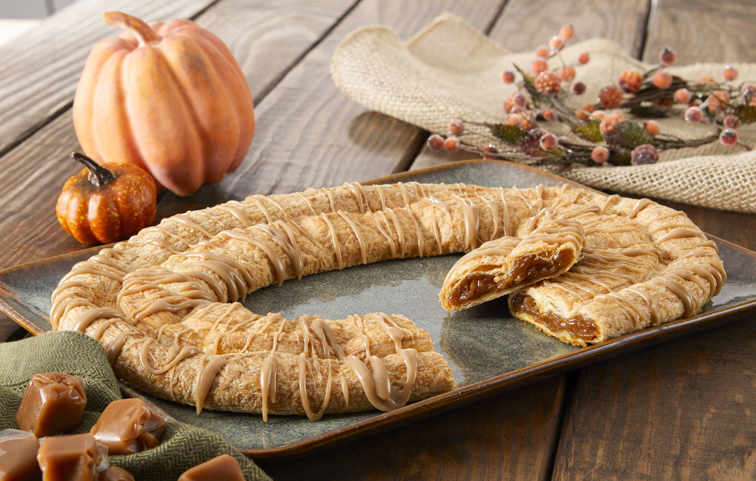 Pumpkin Caramel Kringle sitting on a grey plate with a pumpkin and caramel cubes near the kringle.
