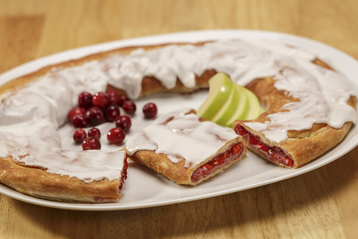 Cranberry Apple Kringle sitting on a white plate with cranberries and green apples near the Kringle.