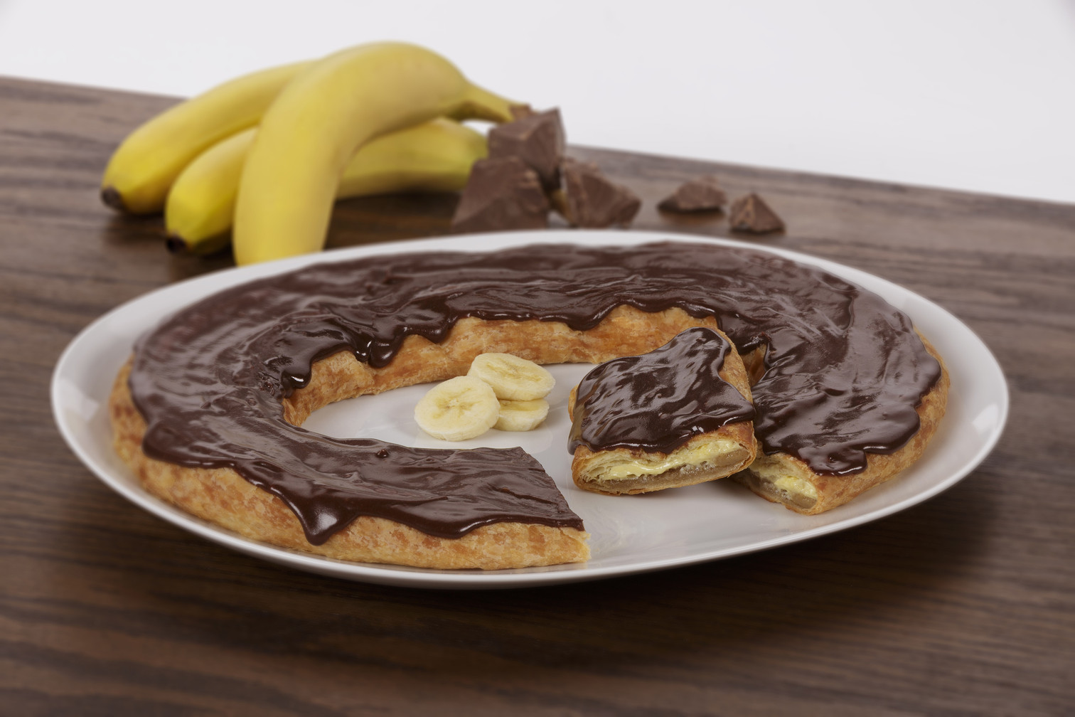 Chocolate Banana Kringle sitting on a white plate with a couple of banana slices near the Kringle.