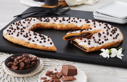 Chocolate Chip Kringle on black slate plate with a bowl of chocolate chips and chunks of chocolate near the kringle.
