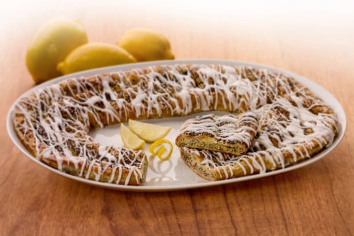 Lemon Poppyseed Kringle on a white plate with some lemon slices and lemons near the Kringle.