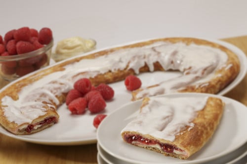 Raspberry Cheesecake Kringle on white plate, slice on smaller plate surrounded by raspberries.
