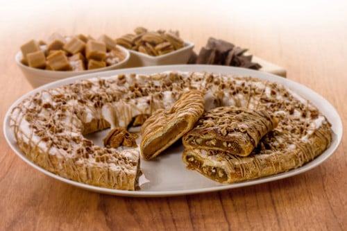 Turtle, Praline Pecan, Sea Salt & Caramel Kringle sitting on a white plate with a couple of pieces cut out.