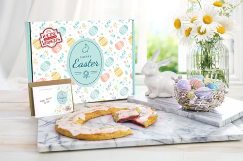 Easter Gift Box with a Kringle on a marble cutting board in front of the box with a ceramic white rabbit and some colored eggs near the Kringle.