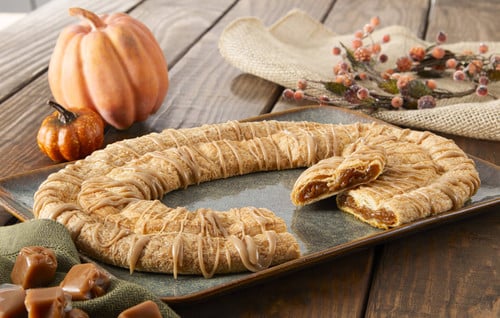 Pumpkin Caramel Kringle sitting on a grey plate with a pumpkin and caramel cubes near the kringle.
