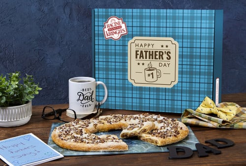 Father's Day Gift Box Kringle with a Bourbon Pecan Kringle in front of the box with some coffee and a bow tie near the kringle.