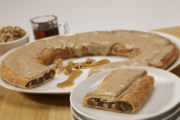 Maple Walnut Kringle on white plate along with syrup drizzled on walnuts.