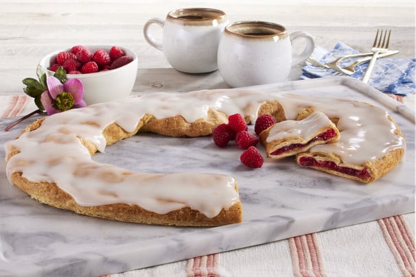 Raspberry Kringle sitting on a marble cutting board with raspberries and a mug of coffee.
