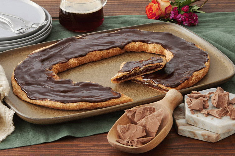 Chocolate Silk Kringle of brown plate with chocolate shavings in a wooden spoon near the kringle.