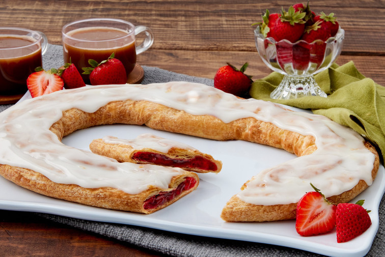 Strawberry Kringle sitting on a white plate with some strawberries and two mugs near the Kringle.