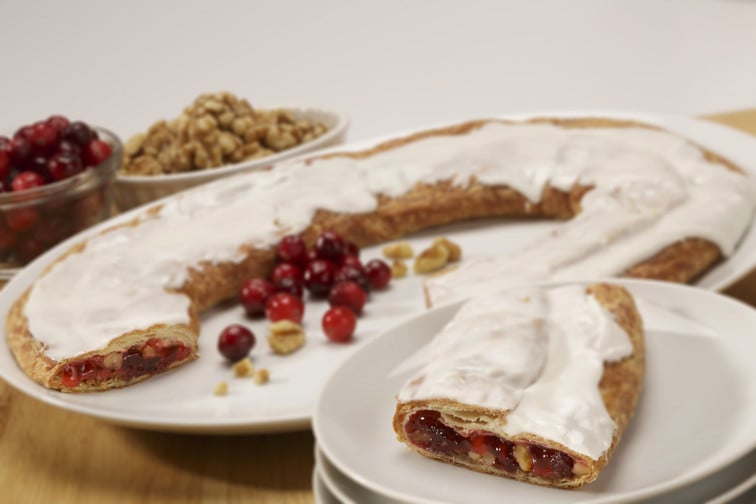 Cranberry Nut Kringle on a white plate with a slice on a smaller plate along with bowls of cranberry and walnuts.