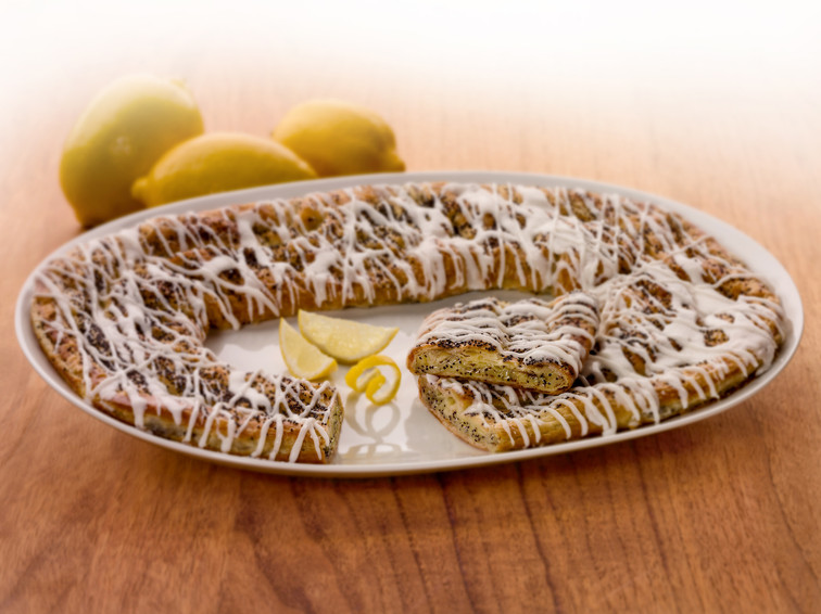 Lemon Poppyseed Kringle on a white plate with some lemon slices and lemons near the Kringle.
