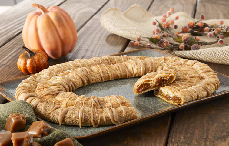 Pumpkin Caramel Kringle sitting on a grey plate with a pumpkin and caramel cubes near the kringle.