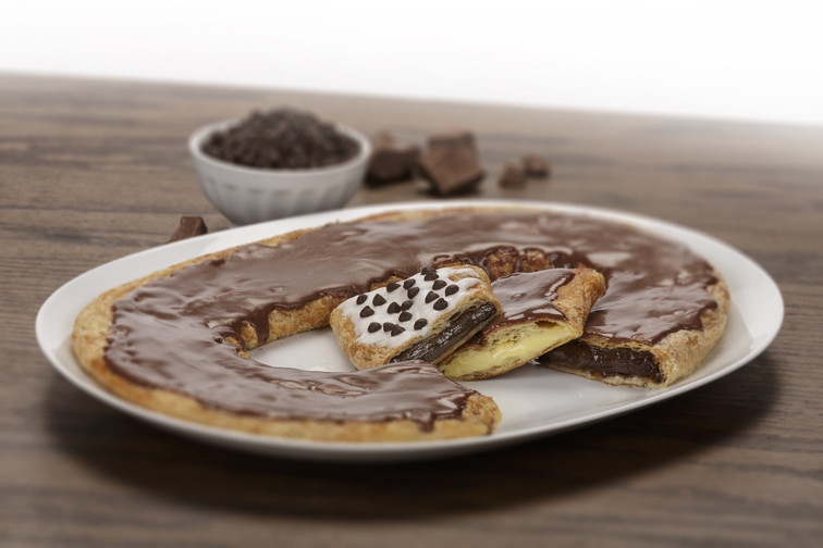 Chocolate Silk Kringle with slices of Chocolate Chip Kringle and Chocolate Eclair Kringle on white plate along with bowl of chocolate chips and blocks of chocolate.