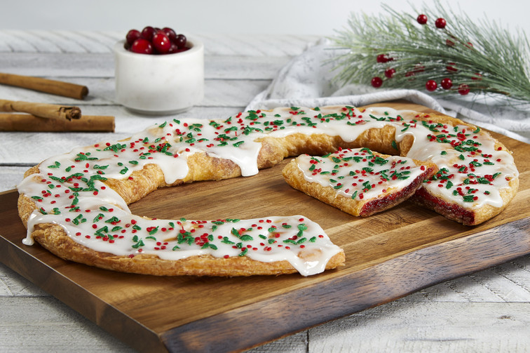 Santa's Cinnaberry Kringle on wood board with bowl of cranberries, cinnamon sticks and festive pine branch.