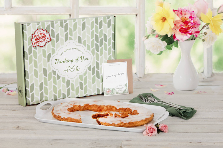 Kringle on a white plate in front of a Thinking of You Gift Box with flowers.