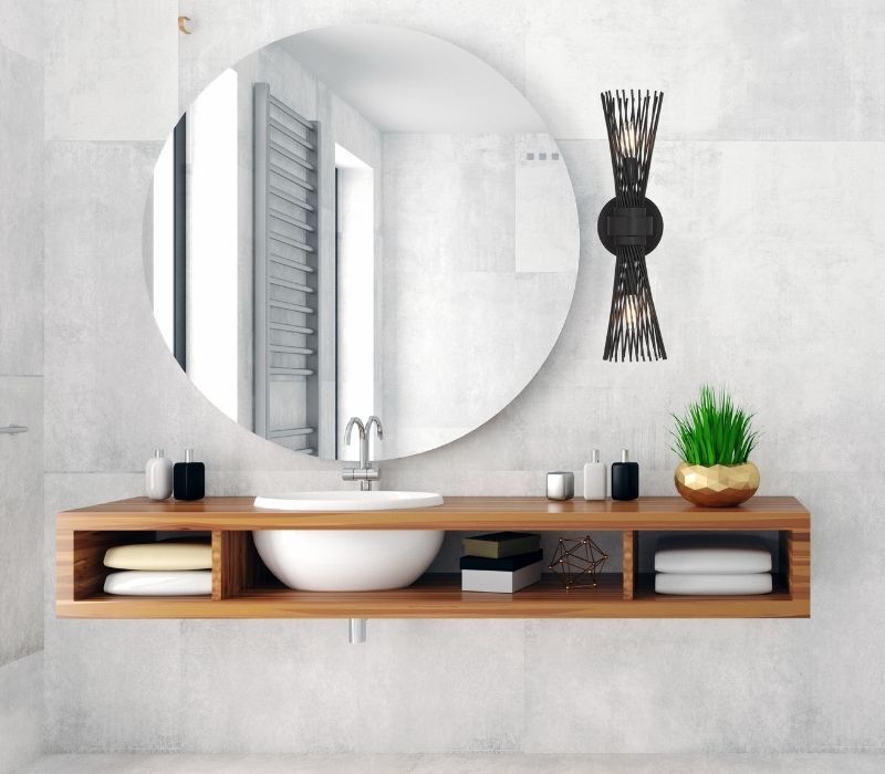 Longfellow 2-Light Wall Sconce styled in a modern bathroom above a floating wooden vanity next to a circular mirror. 