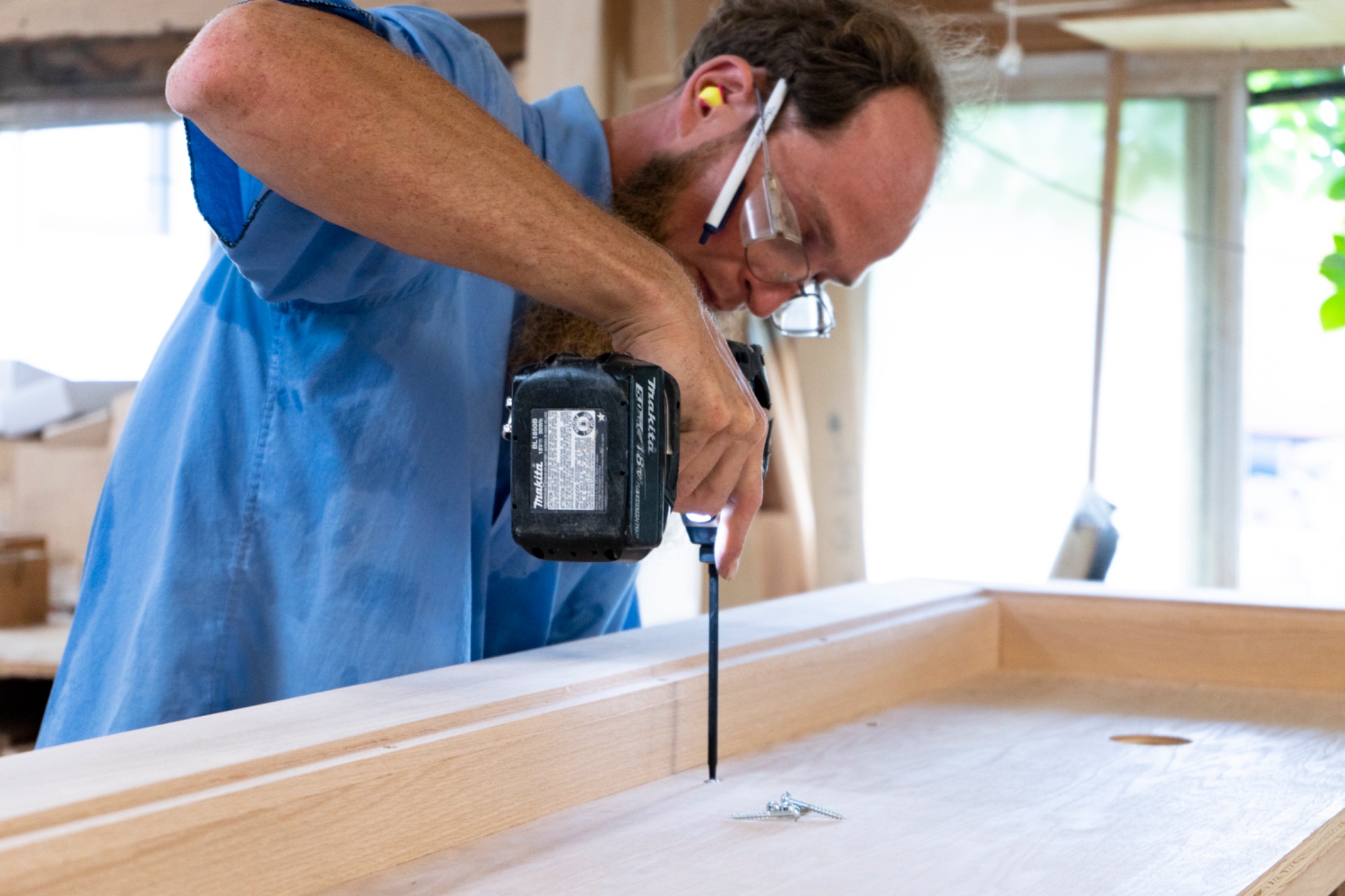 A worker using a handheld driver on a wooden furniture assembly