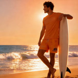 An orange pair of men's polyester spandex swim shorts displayed with a model by the beach, holding a surfboard.