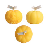 Three pumpkin-shaped candles in vibrant yellow, featuring varying designs, including one with a skull motif.