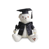 A plush white bear wearing a graduation gown and cap, holding a pen, featuring a logo on its foot.