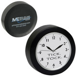 A black quart clock shape stress reliever with a white clock face and black numbers. It features a logo on the back.