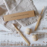 Bambu toothbrushes made from bamboo with white bristles, displayed alongside a cardboard box on a textured linen background.