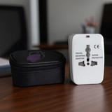 A white travel universal adaptor sits next to a black carrying case, both displayed on a wooden surface.