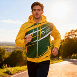 A man wearing a yellow and green men's polyester sublimated training track jacket, jogging outdoors in the sunlight.