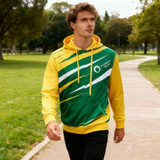 A unisex hoodie featuring green and yellow colours, with a logo, worn by a man walking in a park.