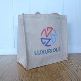 A jute tote bag in a beige hue with a colourful logo on one side. The bag features two sturdy handles.